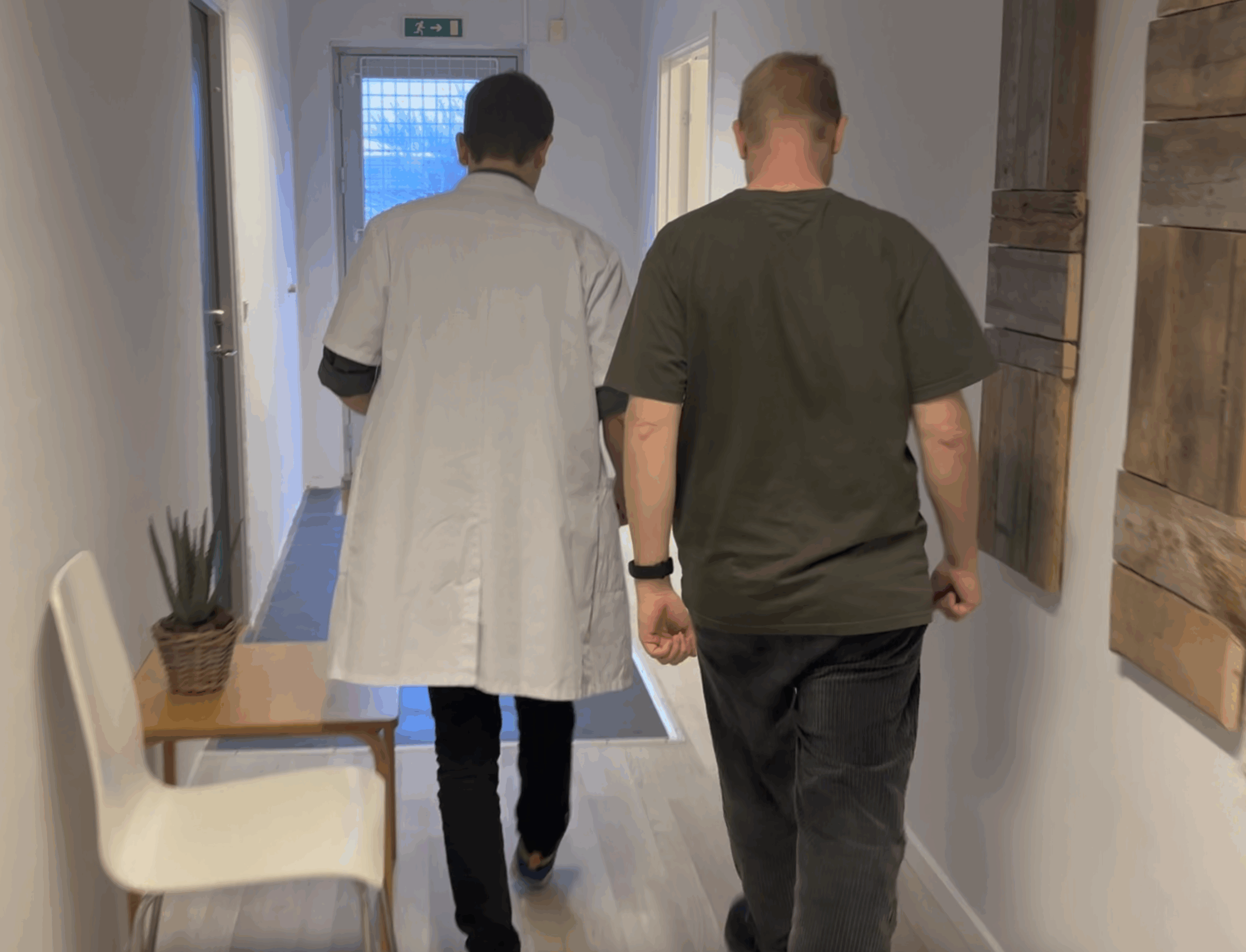 En læge i hvid kittel går sammen med en patient ned ad en korridor i en klinik.