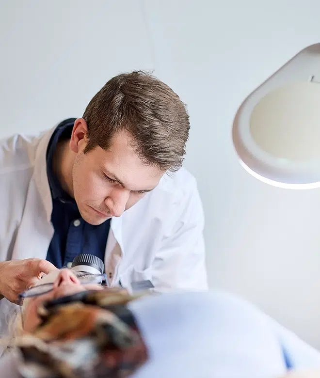 En behandler undersøger en patients hovedbund med en lupe i et klinisk miljø.