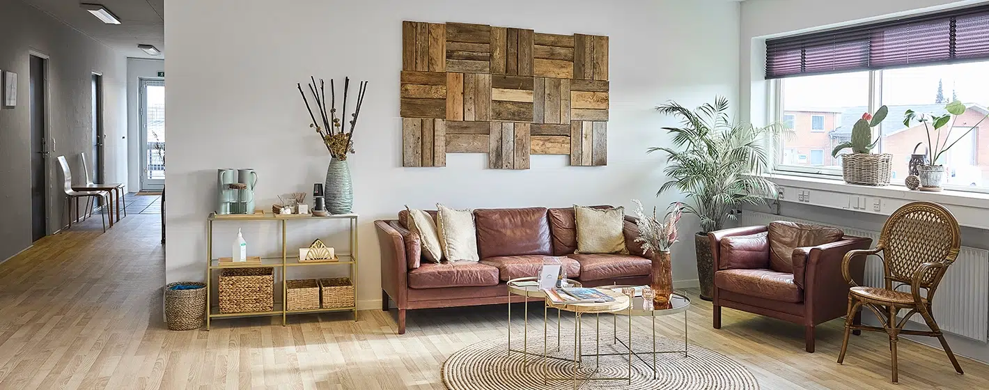 Indretning af et venteværelse med lædersofa, stålbord og dekorative elementer som planter og vægkunst.